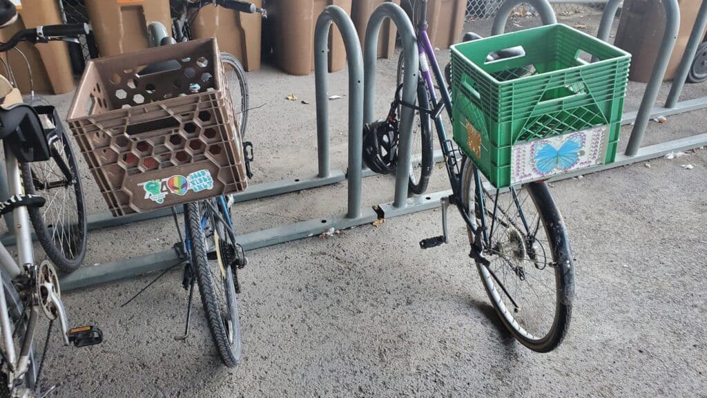 Two parked bicycles with shopping baskets that can be used for grocery shopping without a car